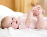 Ein lächelndes Baby von 8 Wochen liegt auf dem Rücken und spielt mit seinen Füßen.
