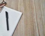 Notatnik, długopis i okulary na drewnianym blacie. Czas na spisanie opinii o uczniu.