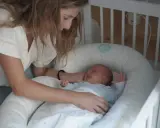 Madre observa a su bebé recién nacido, listo para sus siestas. El pequeño sonríe en su nido acogedor.