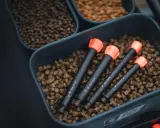 Zanęta halibut na jakie ryby? W pojemniku z pelletem leżą cztery sygnalizatory brań z pomarańczowymi końcówkami.