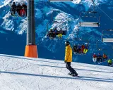 Snowboarder na stoku pod kolejką linową z narciarzami.