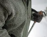 En person i lager på lager-principen lager 2, en grön fleecetröja täckt av snö, håller i en skidstav.
