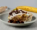 Pyszny sernik banoffee z bananami, karmelem i bitą śmietaną, posypany czekoladą. Obok leży dojrzały banan.