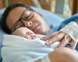 Mutter mit Neugeborenem im Arm, die sich von der Geburt erholt. Die Frage "Wochenfluss wie lange" beschäftigt viele Frauen nach der Entbindung.