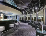 A modern bar with a curved counter, stools, lounge seating, and a patterned carpet.