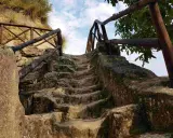 Antica scala in pietra scavata nella roccia, con ringhiera in legno, che conduce verso l'alto, evocando un'esplorazione in una grotta in Calabria.