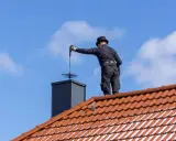 Kominiarz na dachu czyści komin. Zastanawiasz się, ile kosztuje przegląd kominiarski?