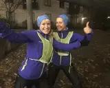 Två glada löpare i blå jackor och reflexvästar ger tummen upp, redo för ett maraton.