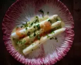 Vitt sparris med en krämig sås, toppad med kaviar och gräslök, serverad på ett rött endiveblad. En delikat ansa sparris.