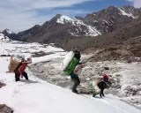 Ludzie niosący ciężkie ładunki w śniegu, zbliżając się do mount everest base camp. Góry w tle.