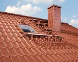 Neues rotes Ziegeldach mit Dachfenster und Schornstein. Informieren Sie sich über die scheunendach erneuern kosten.