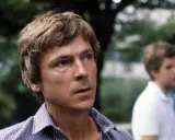 Carl Ivar Nilsson, en man med rufsigt hår och en randig skjorta, tittar bort. En annan man syns suddigt i bakgrunden.