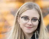 Uśmiechnięta blondynka w okularach, z rozmyciem tła. Idealna ogniskowa do portretu, podkreślająca oczy.