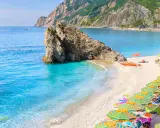 Ein malerischer italien strand mit türkisfarbenem Wasser, einem Felsen im Meer und vielen bunten Sonnenschirmen.