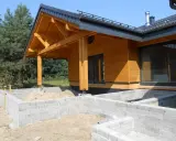Drewniany dom w budowie, z widocznym fundamentem z bloczków betonowych i dachem o kącie nachylenia 12 stopni.