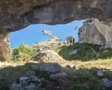 Vista desde el "ojo del diablo", una cueva natural, hacia un paisaje costero con un istmo y el mar azul. Un grupo de personas observa el panorama.