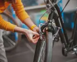 Osoba w żółtym swetrze dokonuje wymiany klocków w rowerze, dbając o sprawne hamulce.