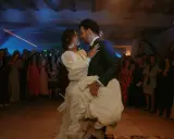 Novios bailando su vals boda, rodeados de invitados expectantes. La novia, con un vestido blanco voluminoso, es alzada por el novio.