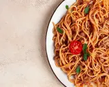 Pyszne spaghetti z mięsem mielonym, udekorowane pomidorkiem i listkami bazylii. Idealne na szybki obiad.
