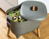Compostador gris con restos de comida y hojas. Aprende como hacer compost para un jardín sostenible.