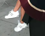 White New Balance dad shoes with a black "N" logo, paired with a pleated skirt.