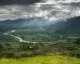 Ein gewundener Fluss schlängelt sich durch ein grünes Tal in Costa Rica. Wolken ziehen über die Berge, die das Bild umrahmen.