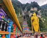 Kolorowe schody Batu Caves w Malezji, prowadzące do jaskini, obok złotej statuy boga Murugana. Warto zobaczyć!
