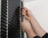 Ręce próbują opuścić czarną roletę zewnętrzną, która zacina się przy opuszczaniu.