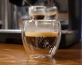 Ein dampfender doppio macchiato in einem doppelwandigen Glas mit einem Eichhörnchen-Motiv.