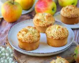 Trois muffins pomme amande dorés avec un crumble croustillant, entourés de pommes fraîches sur une table en bois.