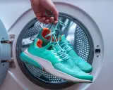 Türkisfarbene Laufschuhe werden vor dem Waschen in der Waschmaschine gehalten.