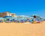 Słoneczny dzień na plaży w Lido di Jesolo. Rzędy leżaków i parasoli w niebiesko-białe pasy czekają na plażowiczów.