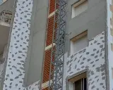 Proceso de como aislar una pared ya construida con placas de poliestireno y mortero. Se observa una grúa de obra.