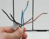 Main d'une personne tenant des fils dénudés d'un radiateur électrique. Une étiquette indique "Pilot wire Black".