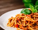 Pyszne spaghetti z bogatym sosem mięsnym, posypane parmezanem i udekorowane świeżą bazylią. Idealny sos do spaghetti na obiad.