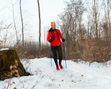 Kobieta w lesie zimą, ćwicząca nordic walking. Końcówki do kijków nordic walking zapewniają stabilność na śniegu.
