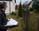 Mężczyzna z dokumentami analizuje teren, szukając sposobu, jak podważyć zasiedzenie. Sąsiad obserwuje go zza płotu.