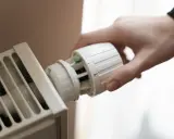 Hand dreht Thermostat einer Heizung. Energie sparen für die Gasheizung 2026.