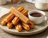 Montón de churros sin gluten espolvoreados con azúcar, junto a una taza de chocolate caliente.