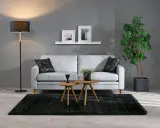 En stilren inredning grått med en ljusgrå soffa, svart matta och en golvlampa. Två runda bord framför soffan.