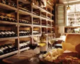 Regal gefüllt mit italienischem Wein, daneben Gläser mit Rot- und Weißwein, Käse und Brot auf einem Holztisch.
