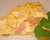 Une omelette jambon fromage dorée, garnie de dés de jambon rose et de fromage fondant, accompagnée de quelques feuilles vertes.