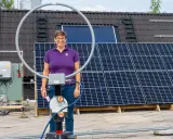 Kvinna med glasögon står framför solpaneler. Ett solceller montagesystem är synligt på taket.