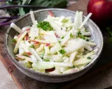 Kohlrabi Salat mit Apfelstücken und frischer Petersilie, garniert mit einem roten Apfel im Hintergrund.