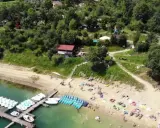 Polańczyk plaża tętni życiem. Ludzie odpoczywają na piasku, a na wodzie czekają rowery wodne i kajaki.