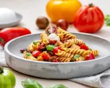 Ein köstlicher italienischer Nudelsalat mit Fusilli, Tomaten, Mozzarella und Basilikum auf einem grauen Teller.