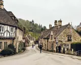Kamienna uliczka w Cotswolds z tradycyjnymi domami i ludźmi spacerującymi po drodze.