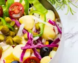 Ensalada campera vibrante con patatas, tomates, pepinillos, pimientos verdes, cebolla morada y aceitunas negras en un bol metálico.