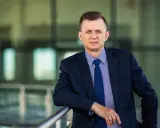 Mężczyzna w garniturze i krawacie opiera się o barierkę.
