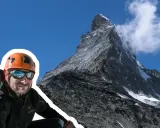 Uśmiechnięty alpinista w kasku i goglach na tle majestatycznego Matterhornu. To jego wejście na Matterhorn, cel zdobyty!